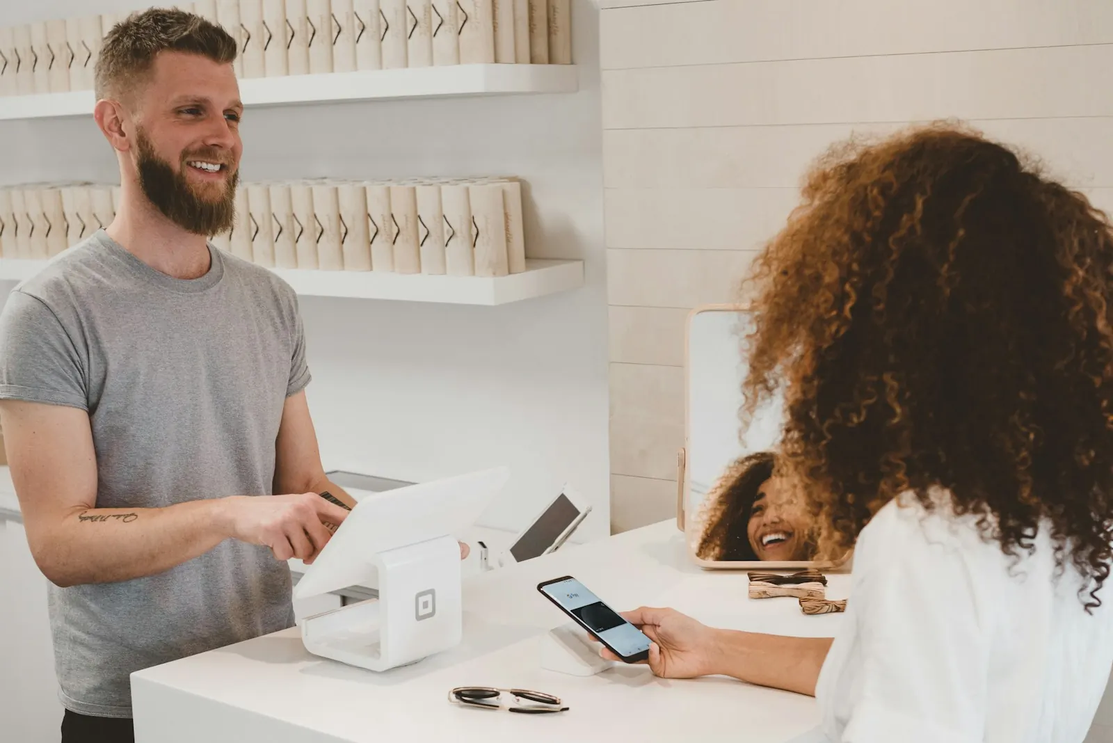 A shop owner serving a customer who pays by phone at the counter